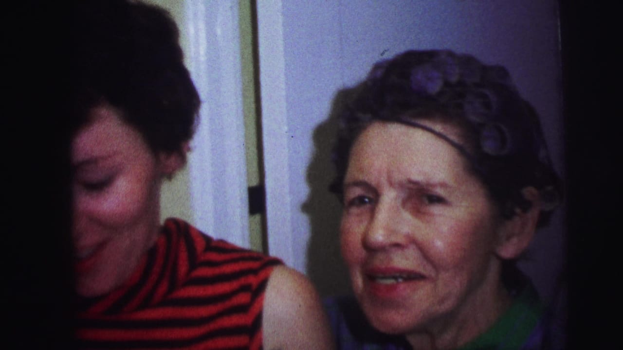 1973 Lynbrook 8mm frame showing a younger woman partly turned down and an older woman in hair rollers looking toward camera indoors.