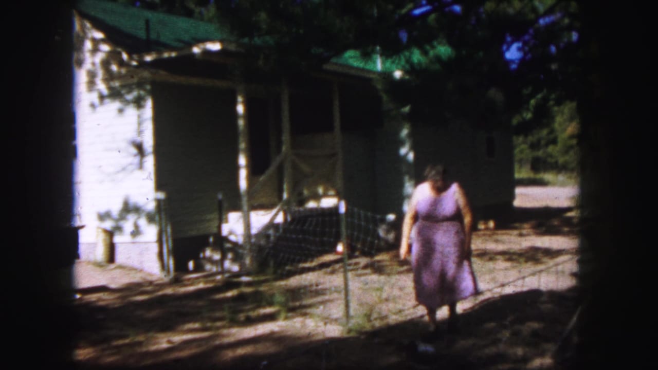 Near the end of the 1958 Colorado Springs clip, the woman passes closer to the camera in the shaded yard outside the house.