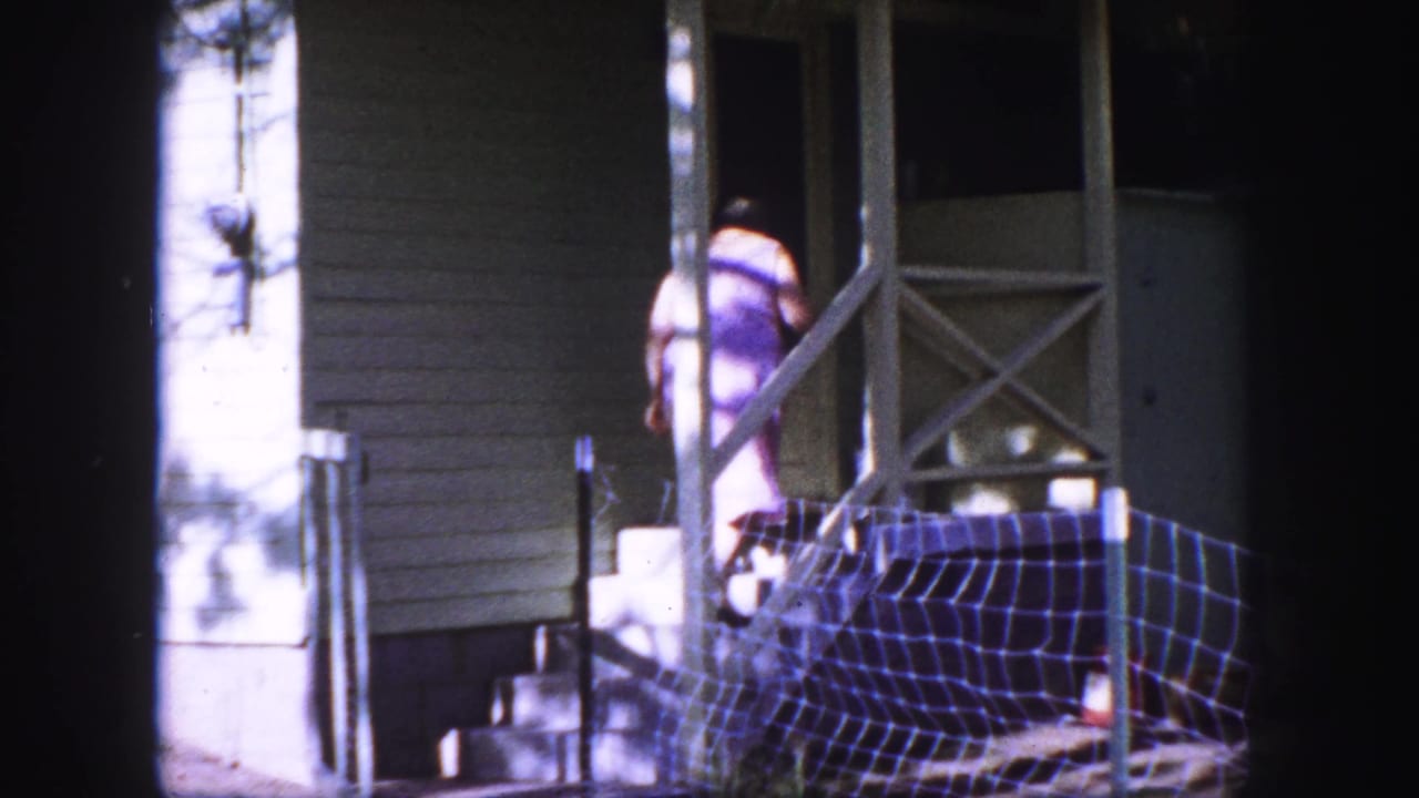 1958 Colorado Springs frame of a woman in a purple dress reaching the porch steps of a small white house.