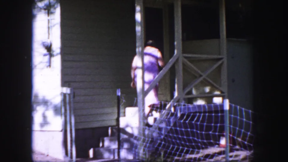 1958 Colorado Springs frame of a woman in a purple dress reaching the porch steps of a small white house.