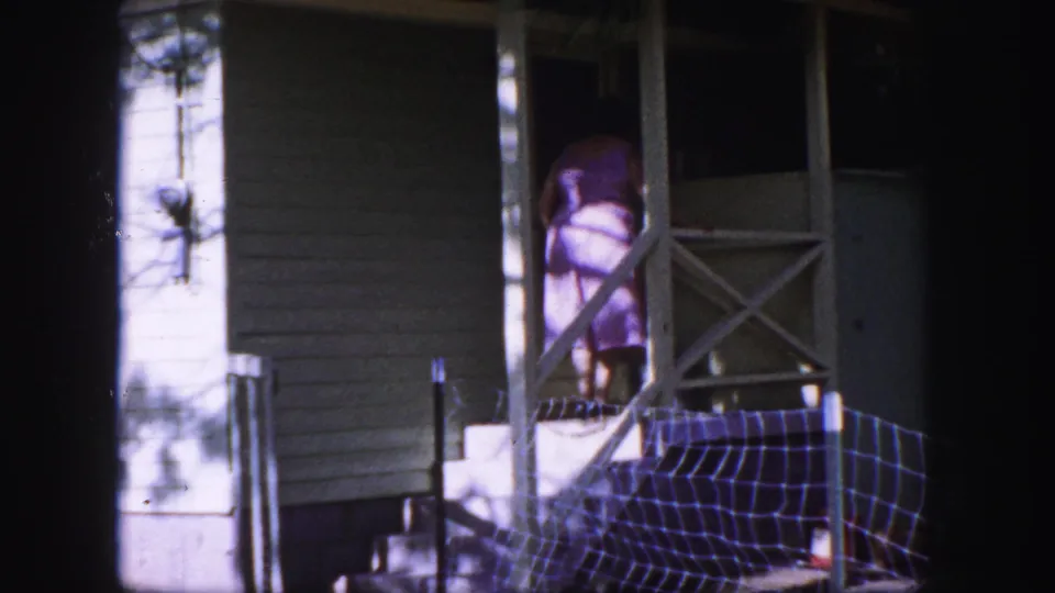 1958 Colorado Springs home-movie frame with the woman on the porch near the railing and dark doorway of the white house.