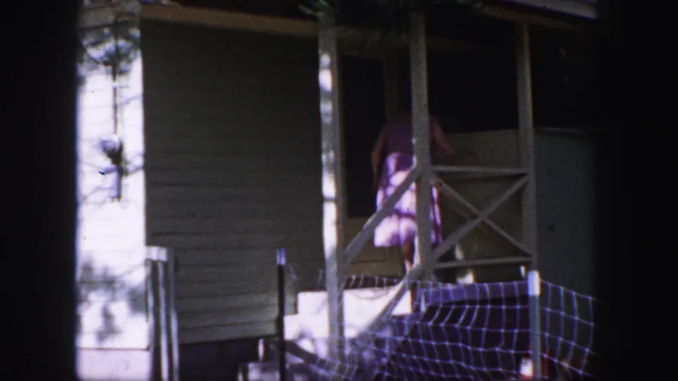 1958 Colorado Springs frame showing the woman at the doorway as she enters from the porch of the small white house.