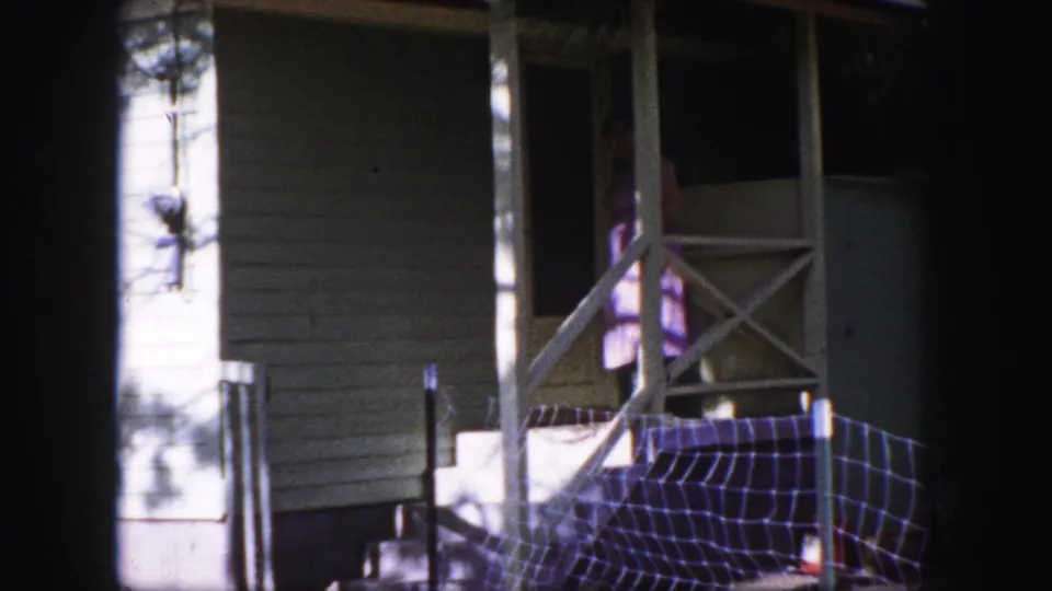 The woman begins opening the screen door on a Colorado Springs porch, with siding, railings, and sunlight visible around her.