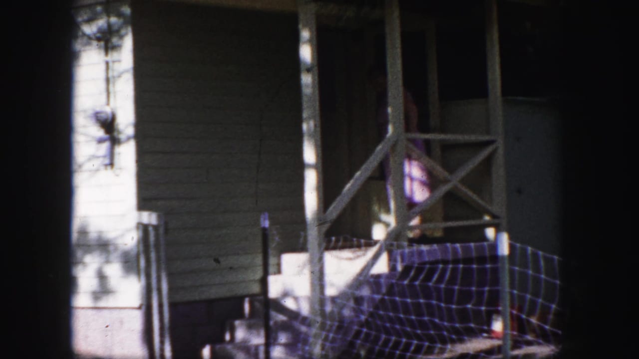 Woman partly visible on a porch beside a front door and cross-braced railing.