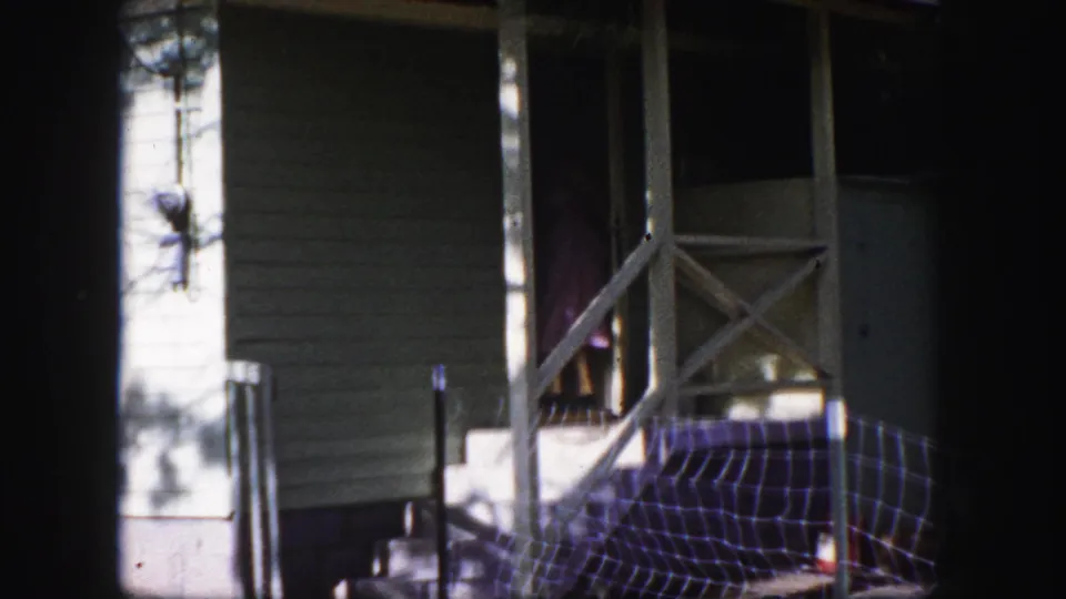 1958 Colorado Springs exterior frame with a woman partly visible on a house porch near railings and blue netting on the steps.