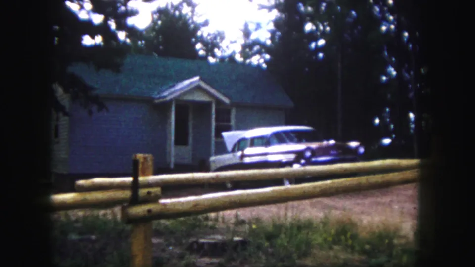 1958 Colorado Springs frame showing a parked 1950s station wagon near a small house, with a split-rail fence and pines in the foreground.