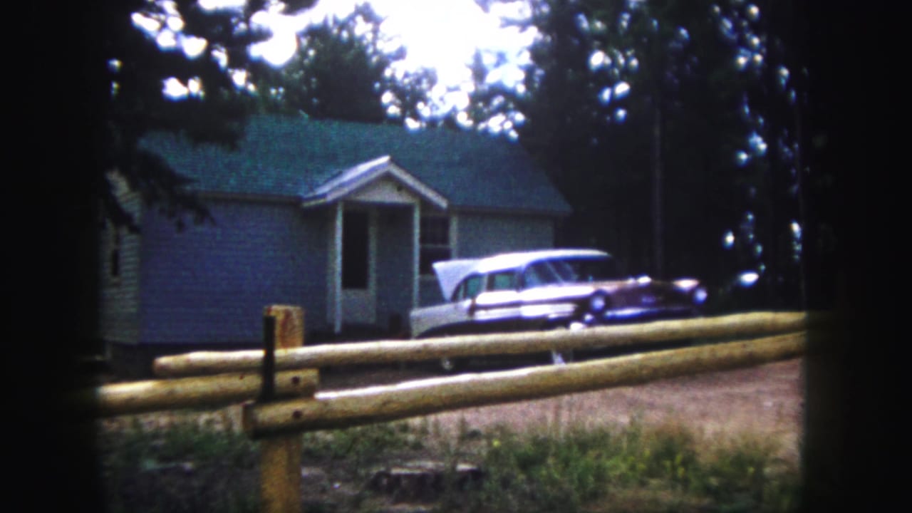 Station wagon parked outside a small house behind a split-rail fence.