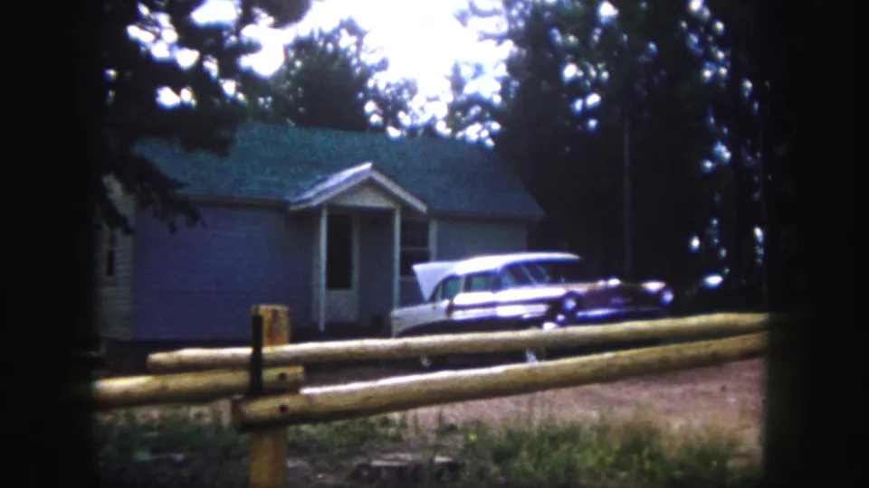 Colorado Springs exterior with a mid-century station wagon beside a blue-sided house in wooded surroundings.