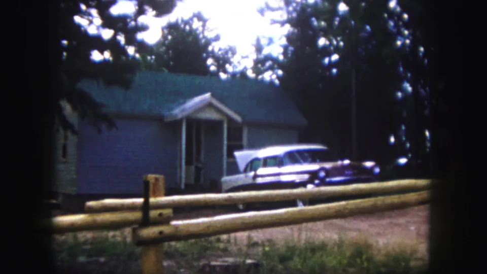 8mm frame of a parked station wagon outside a modest Colorado Springs house, with dark vignette edges.