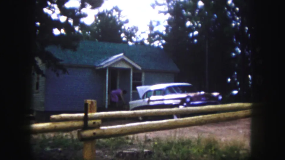 A person in a purple shirt appears near the front door of a Colorado Springs house beside a parked station wagon.