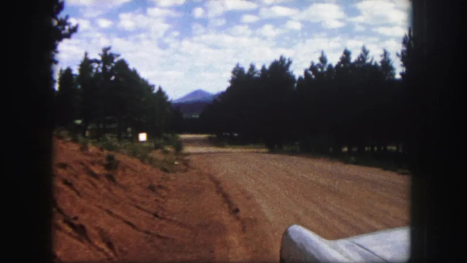 Final 1958 Colorado Springs frame showing the dirt road receding between dark pines toward distant mountains.