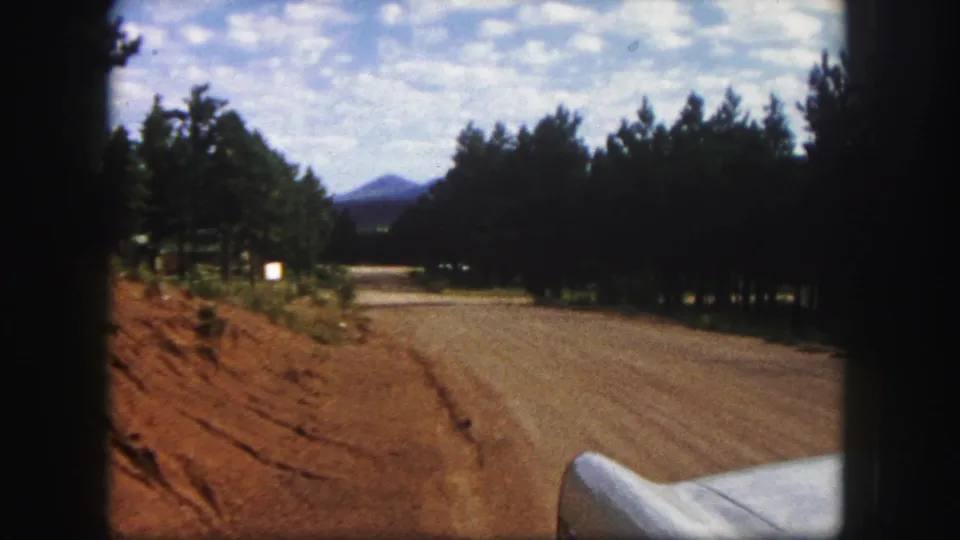 Colorado Springs 1958 home-movie view of a dirt road through pine trees, seen from a car with a distant mountain ahead.
