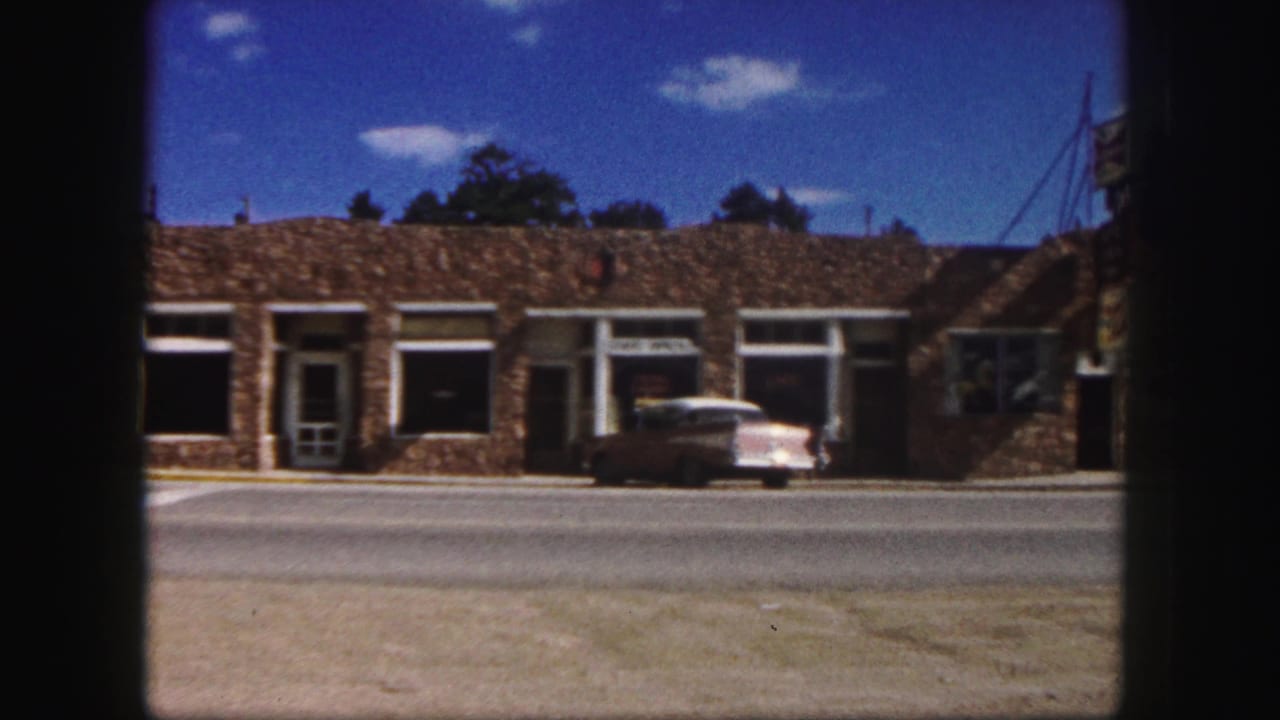Cafe storefront and parked two-tone sedan seen from across the road.