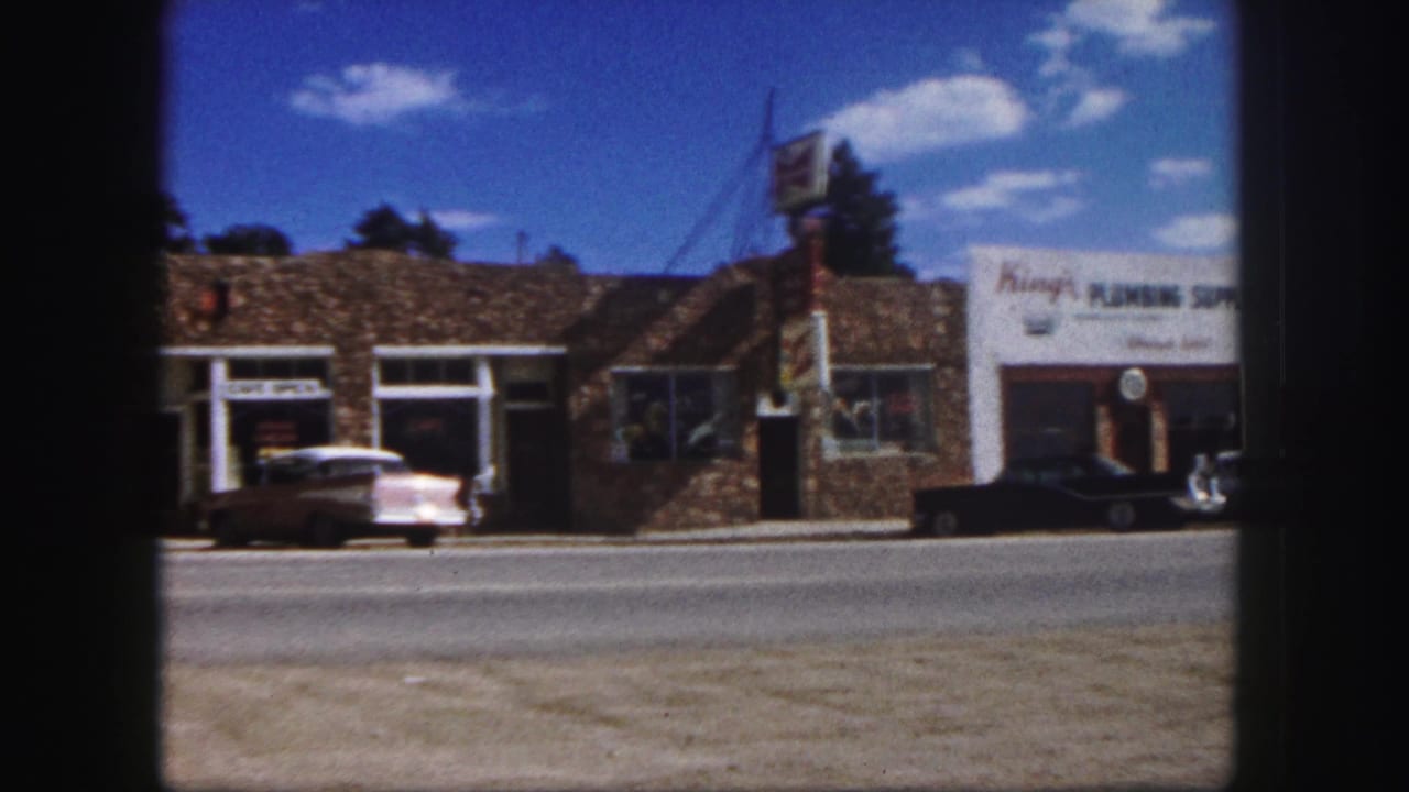 Sunny street with King's Plumbing Supply, parked cars, and neighboring storefronts.