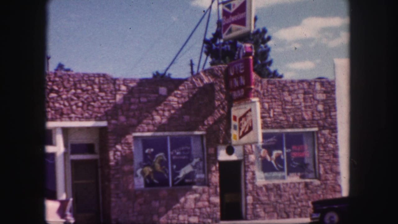 Colorado Springs motel exterior on 8mm film, with stone facing, commercial signage, windows, and a partial parked car.