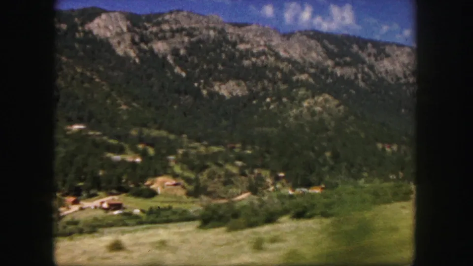 1958 Colorado Springs travel view of wooded mountain ridges, open grass, and scattered valley homes.