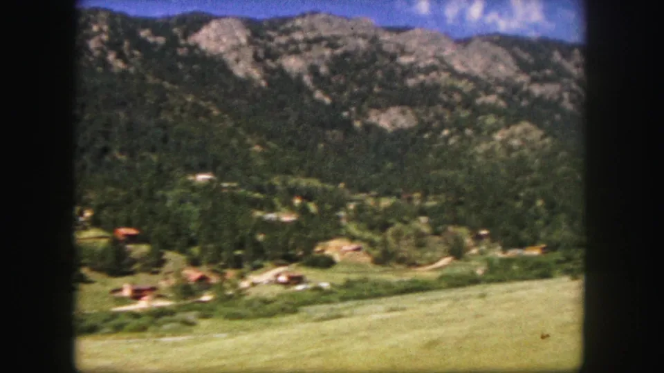 Colorado Springs area landscape on 8mm film, showing wooded ridges, rocky slopes, valley buildings, and grassy foreground.