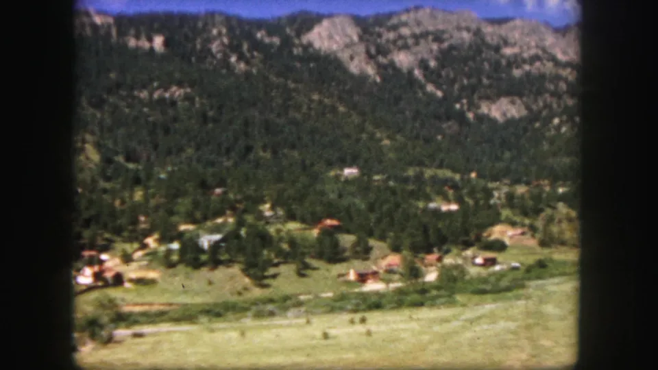 Colorado Springs-area 8mm frame showing scattered valley structures below forested slopes and pale rocky mountain faces.