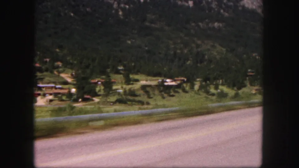End frame of the 1958 Colorado-area road view, with pavement in front and a wooded valley rising toward mountains.