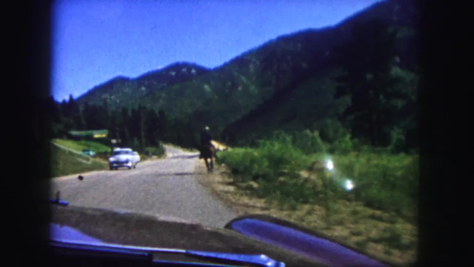 A distant horseback rider moves along the roadside near Colorado Springs as a vintage car passes on a paved mountain road.
