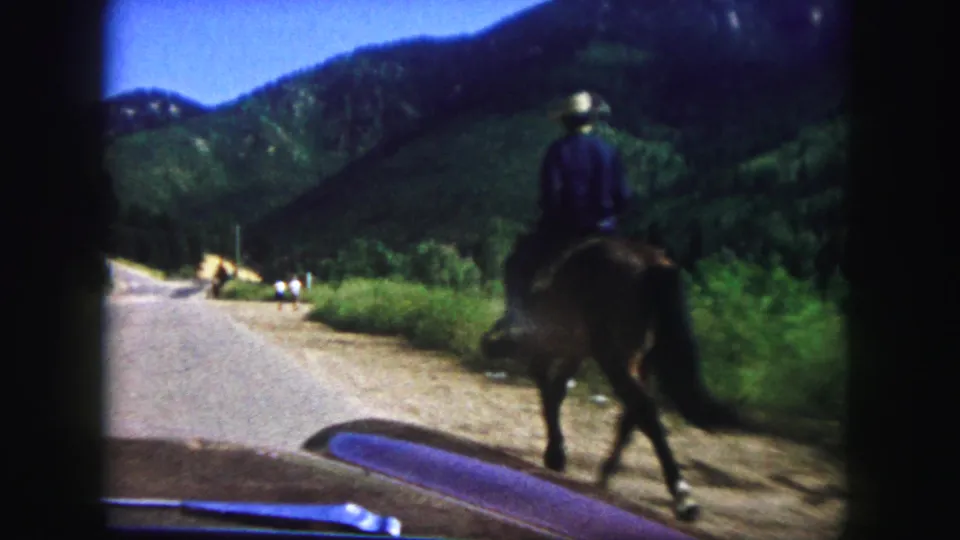 Close 8mm frame of a horseback rider in a hat passing near the camera on a Colorado Springs mountain road in 1958.