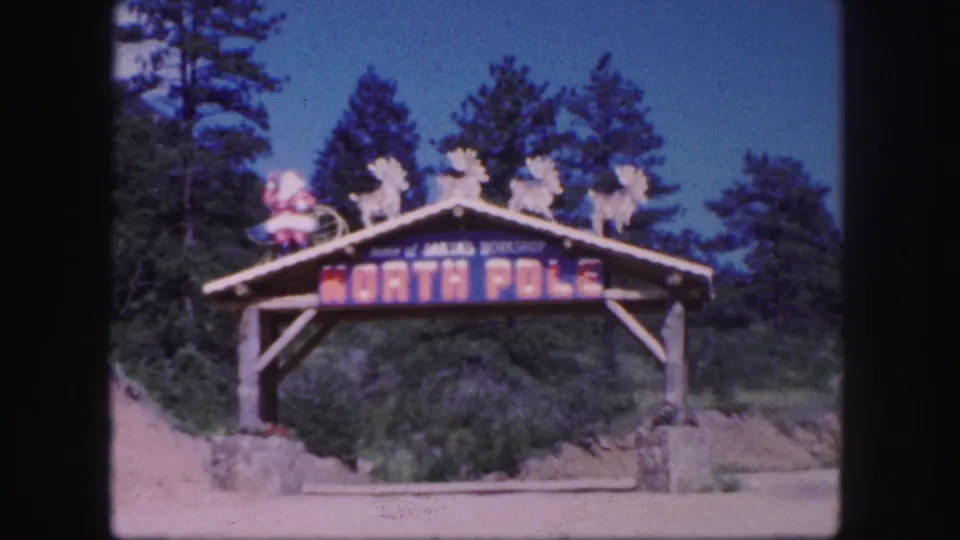 Final 1958 home-movie frame of the Colorado Springs-area North Pole entrance sign set against pine trees and blue sky.