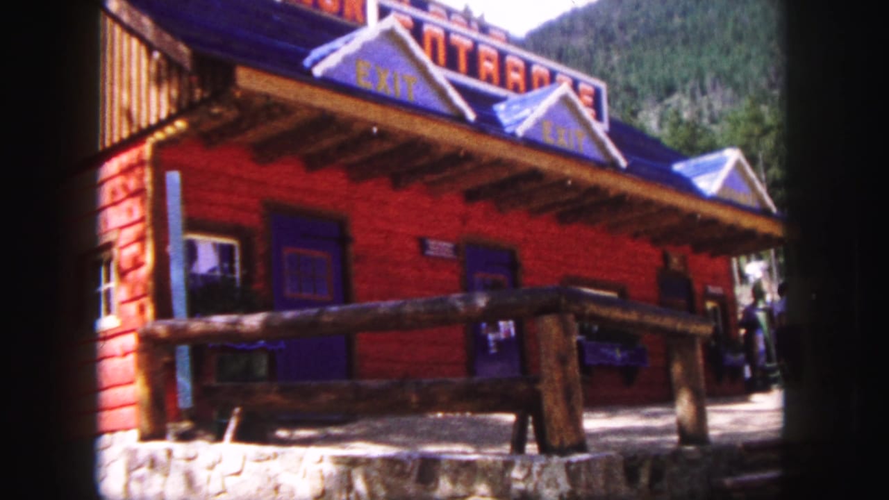 Closer exterior view of the red building, blue roof, log railing, windows, and people at the doorway.