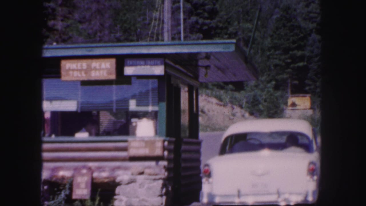 1958 Colorado Springs home-movie frame showing the Pikes Peak Toll Gate booth and a white sedan near the entrance.