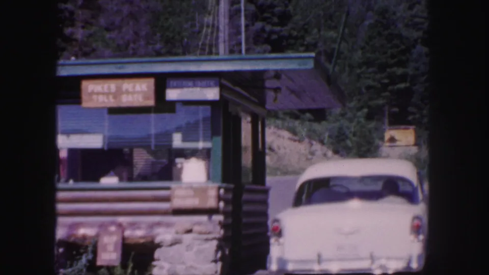 1958 Colorado Springs home-movie frame showing the Pikes Peak Toll Gate booth and a white sedan near the entrance.