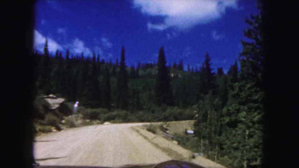 In-car view on a winding dirt road near Pikes Peak, with pine forest and blue sky ahead.