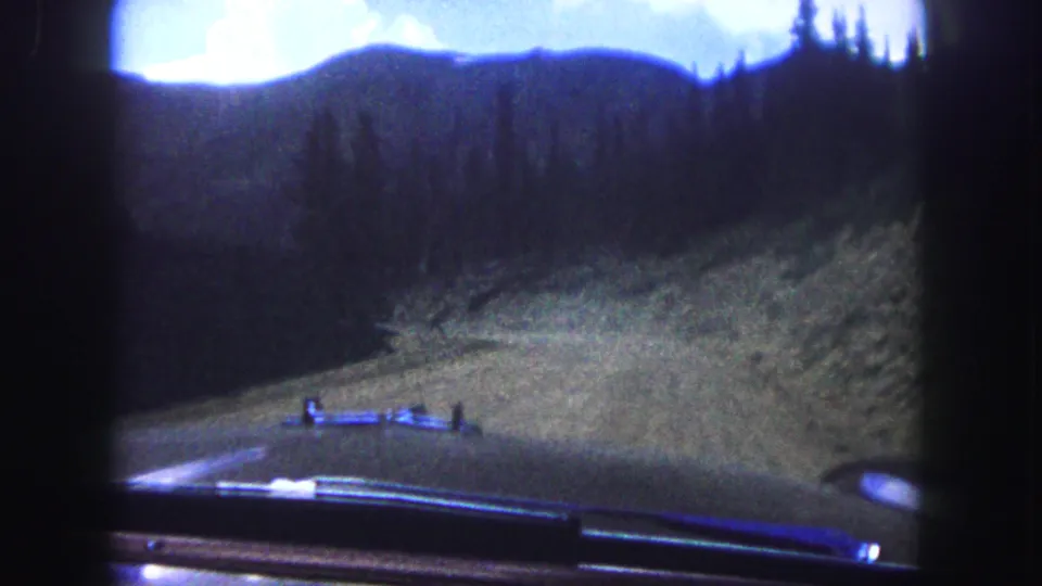 1958 Colorado Springs home-movie frame showing a car's hood below a rough forest road and shadowed mountain ridge.