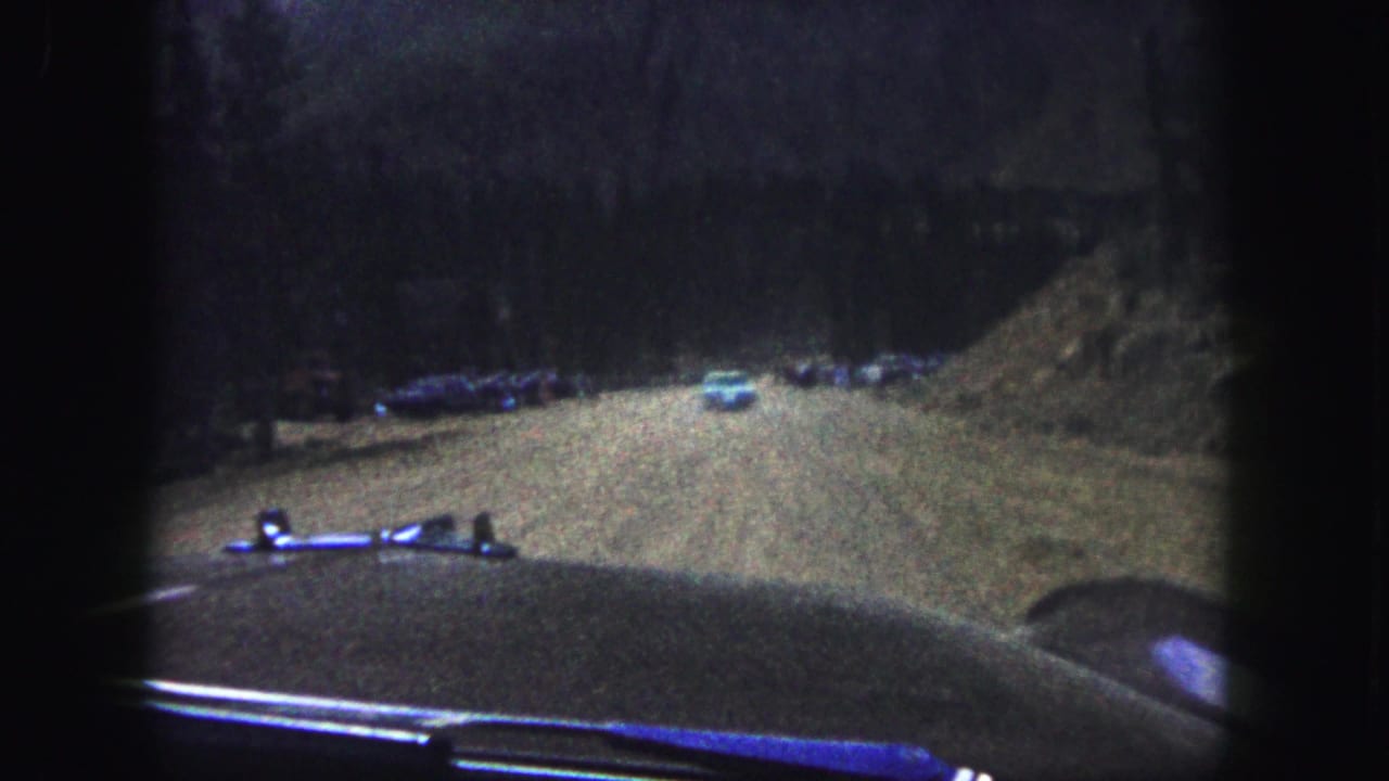 Car approaches a road bend with parked vehicles ahead.