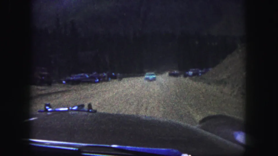 Faded 8mm view from inside a car on a Colorado Springs mountain road, with parked vehicles and forested slopes ahead.