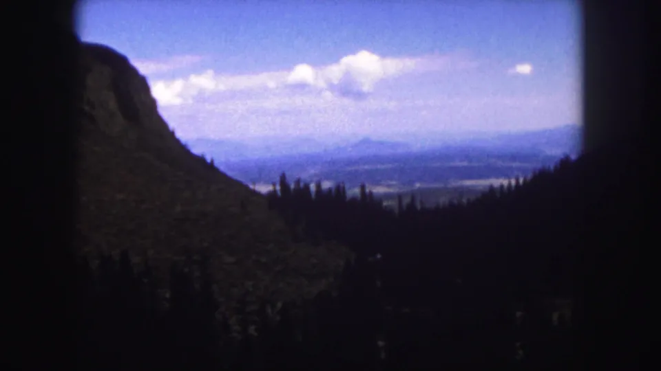 8mm Colorado Springs area vista showing a dark mountain foreground, tree line, distant valley, and pale clouds.