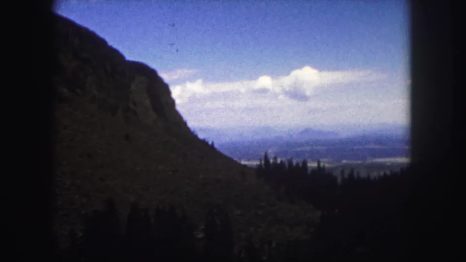 1958 Colorado Springs travel footage frame with a rugged slope, tree line, hazy valley, and dark 8mm frame edges.