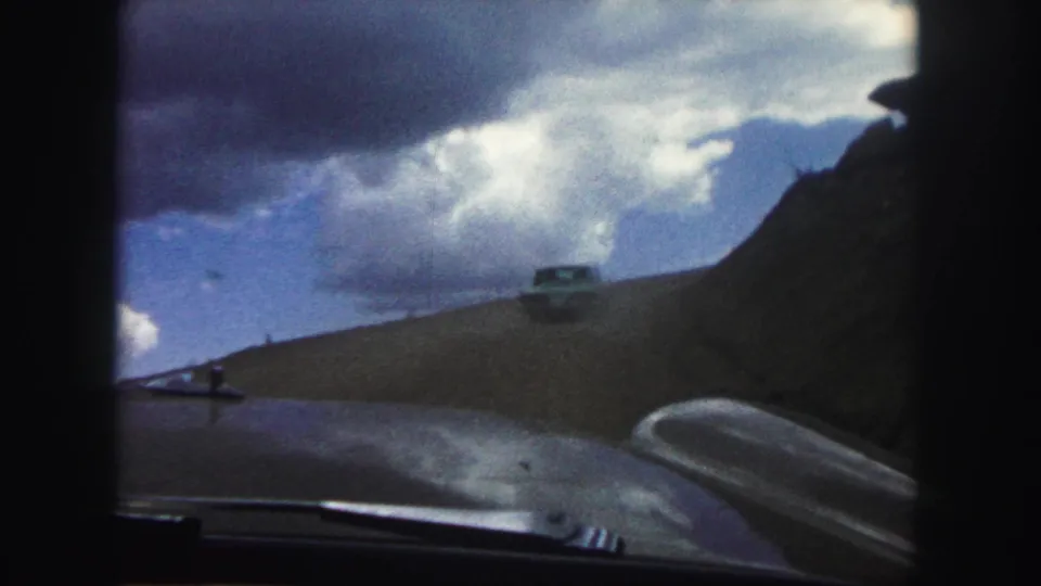 The home-movie camera follows a car up a dirt road in the Colorado Springs area, with hood and sky filling the foreground and background.