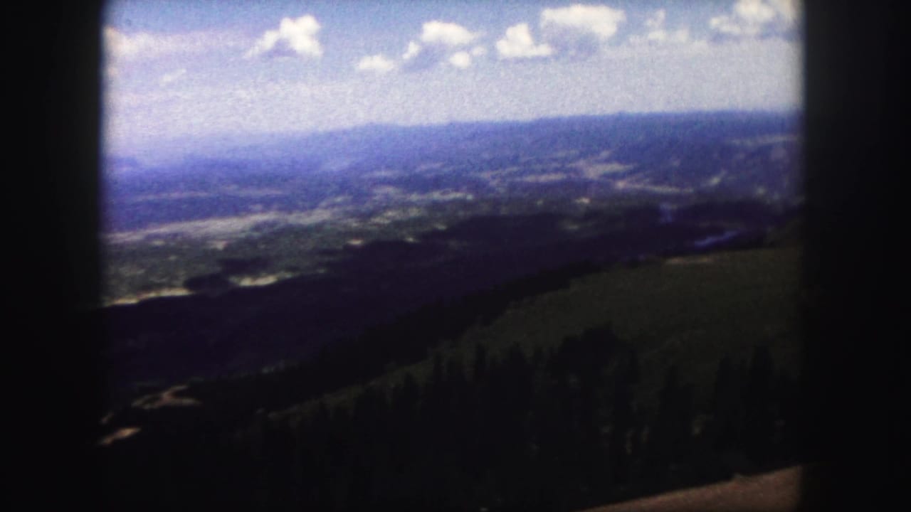 1958 Colorado Springs home-movie frame showing a distant valley beyond forested slopes and open hillside.