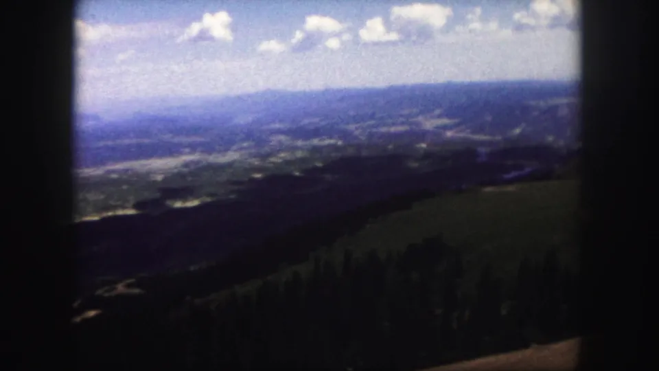 1958 Colorado Springs home-movie frame showing a distant valley beyond forested slopes and open hillside.
