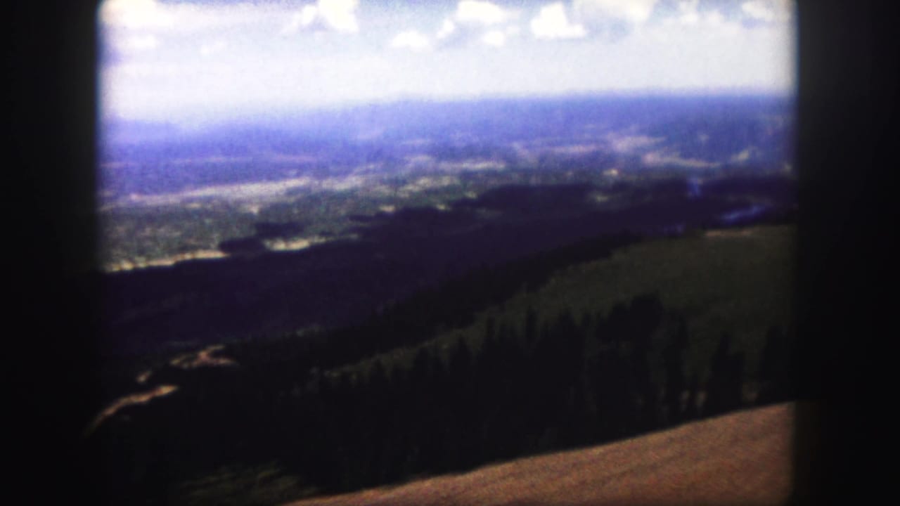 Soft 8mm view of the Colorado Springs area, with dark forested ridges leading toward a broad hazy valley.