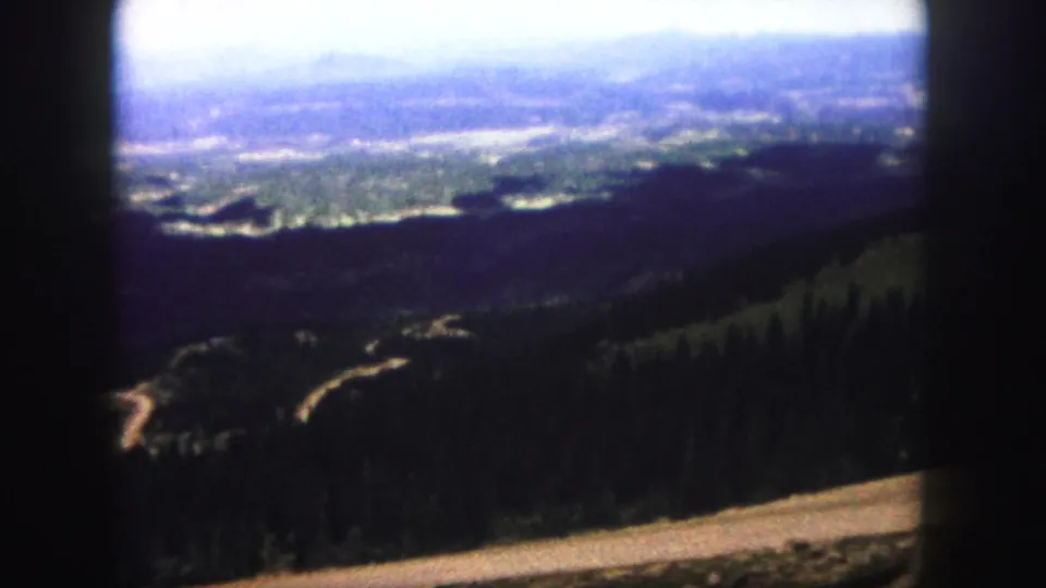 Colorado Springs 1958 home-movie frame looking across forested hills toward a broad sunlit valley.