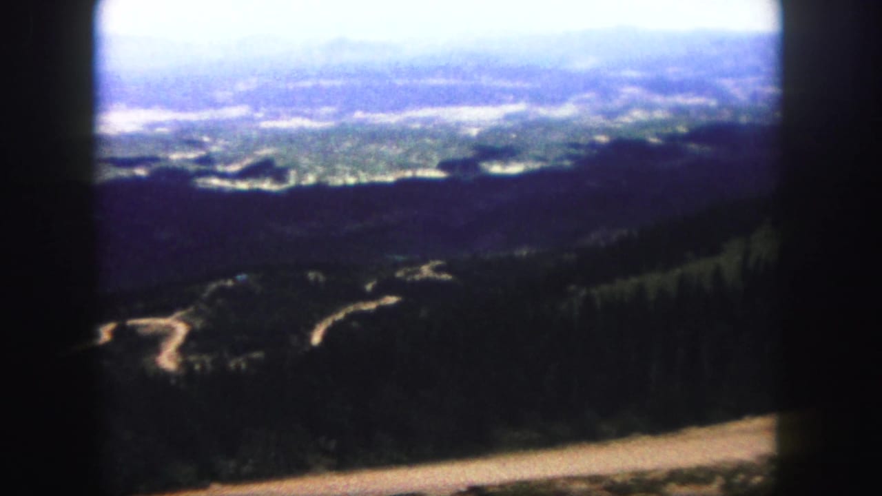 Winding pale road through dark forest below a hazy mountain valley.