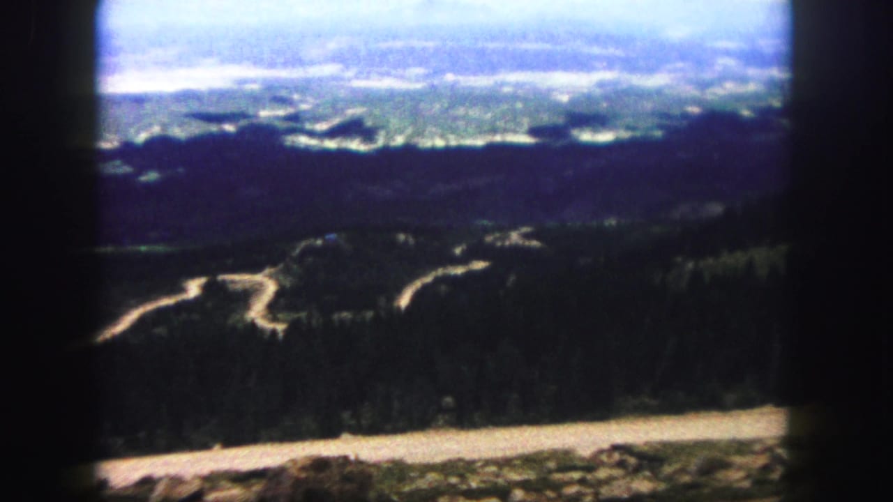 Colorado Springs area mountain view on 8mm film, with curving roads across dark slopes and a pale valley in the distance.