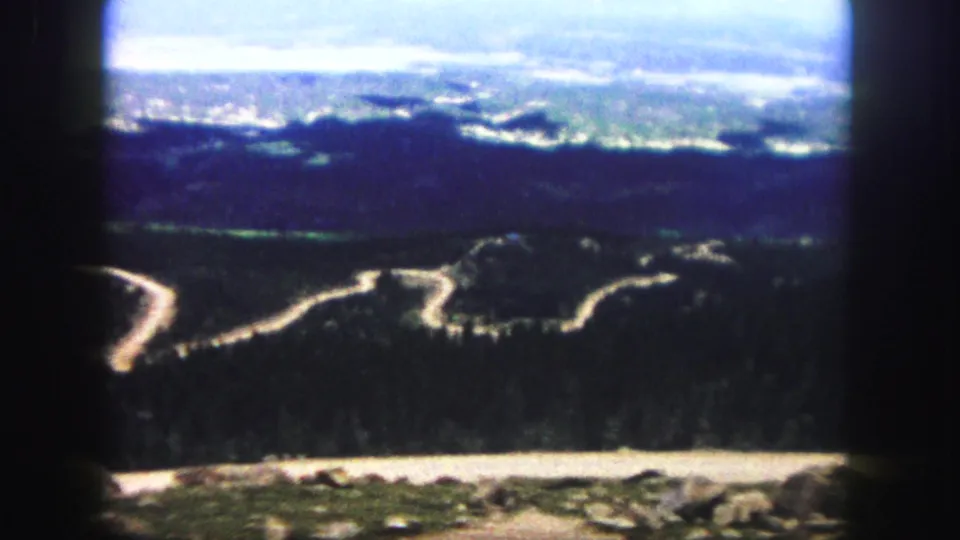 8mm home-movie frame from the Colorado Springs area showing winding mountain roads, dark forest, rocky foreground, and distant haze.