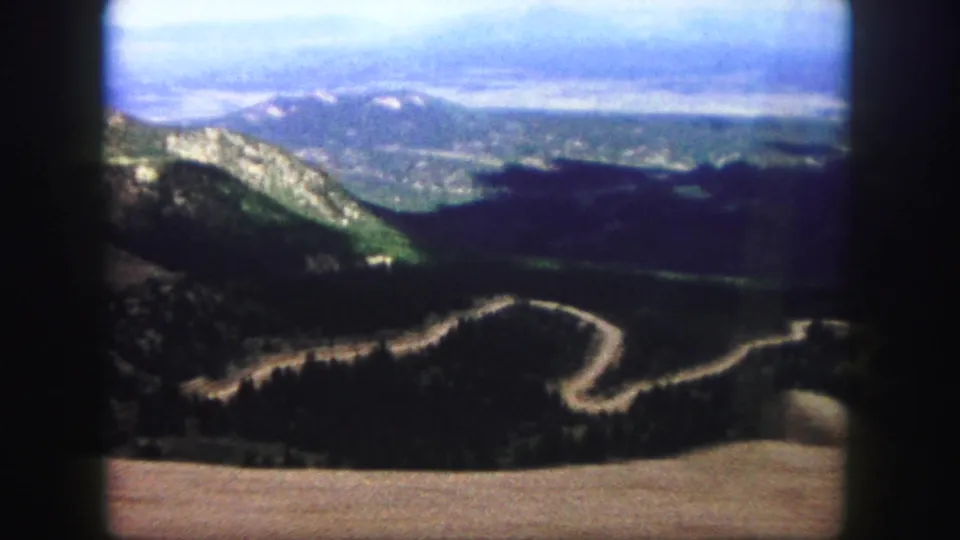 A Colorado Springs-area mountain road curves through wooded slopes in soft, grainy 1958 8mm footage with projector-edge framing.