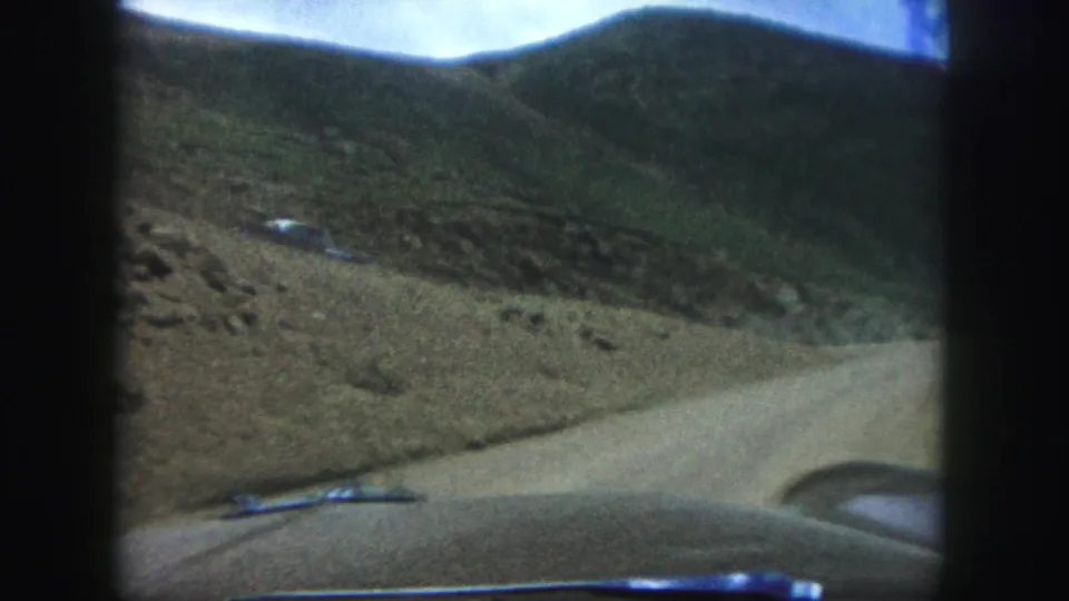 First-person 1958 8mm travel view near Colorado Springs from inside a car, looking toward a dirt mountain road, hillside, and parked vehicle.