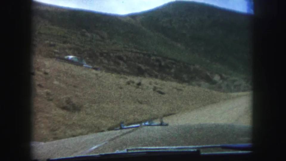 Inside-car view from 1958 Colorado Springs-area home-movie footage, showing dashboard edges, dirt road, sloped hills, and a parked vehicle.