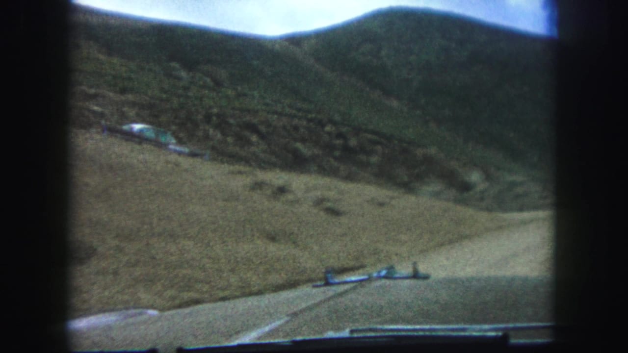 1958 Colorado Springs home-movie view from inside a car on a narrow dirt road below a rocky grass-covered slope.