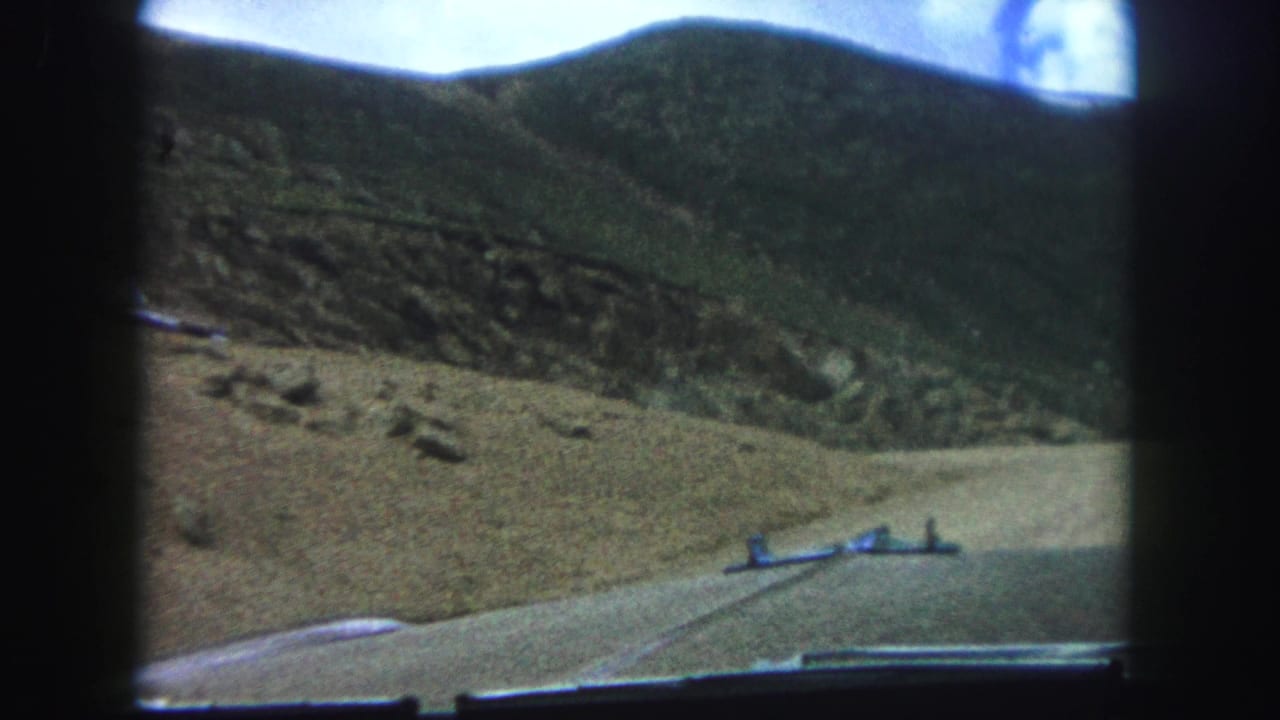 Dirt road curving along a hillside, seen from inside a moving car.