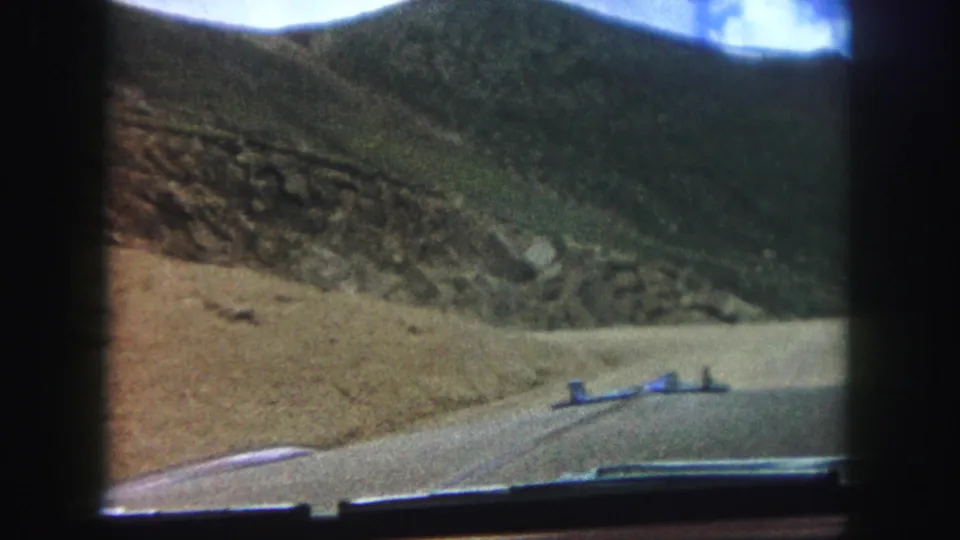 Soft 8mm frame from a 1958 Colorado Springs drive, showing a dirt road, windshield edge, and rocky hillside.