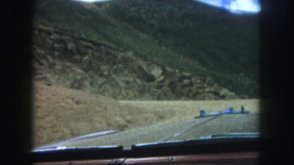 1958 Colorado Springs 8mm driving view with a rural dirt road, car hood edge, and rugged hillside filling the frame.